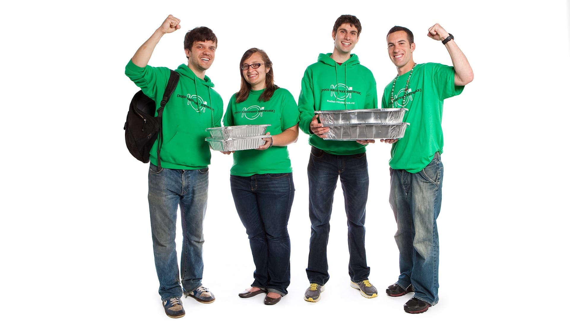 four students from Food Recovery Network cheer while wearing matching green shirts and holding trays of food