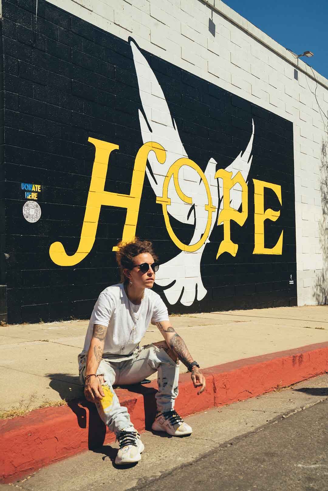 Artist Corie Mattie ’12 sits near mural that reads, "HOPE"