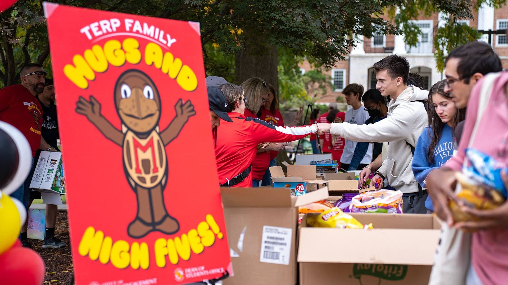 Red sign that says "Terp Family: Hugs and High Fives" with an image of Testudo in front of a table full of snacks