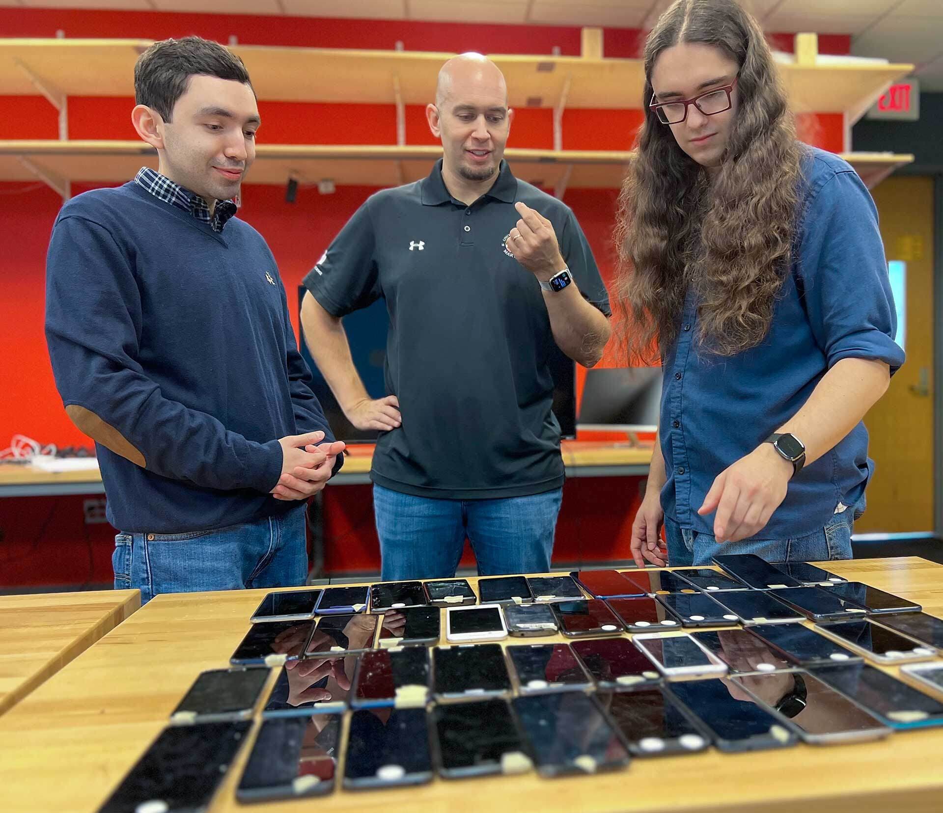 three researchers look at array of old phones on a table