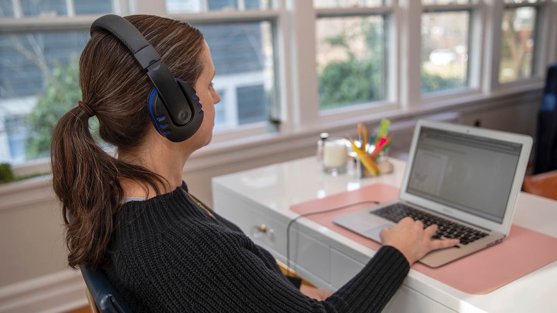 Woman wearing headphones while working on laptop