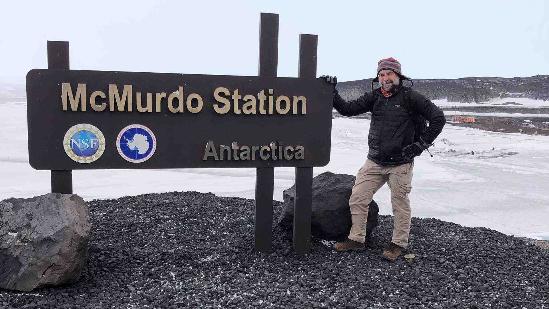 researcher poses next to McMurdo Station, Antarctica sign