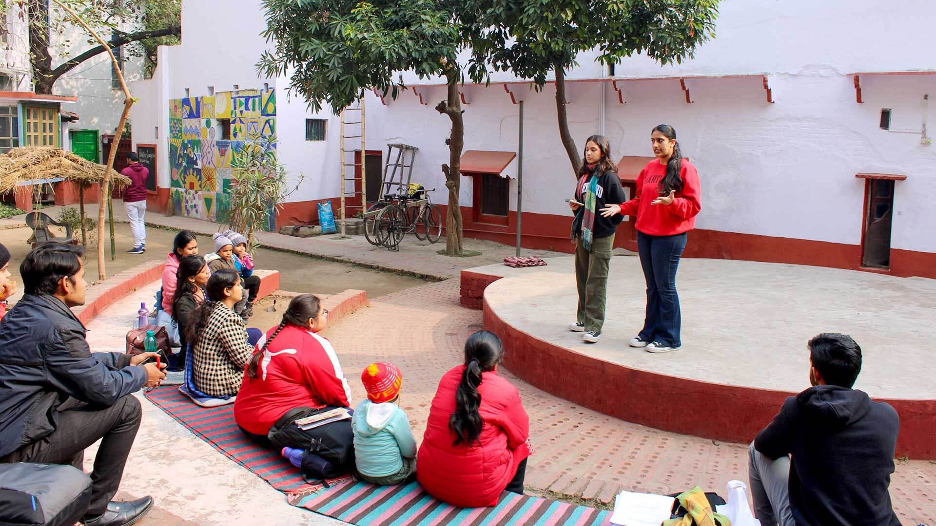 Two women stand on a stage and talk to an audience outdoors