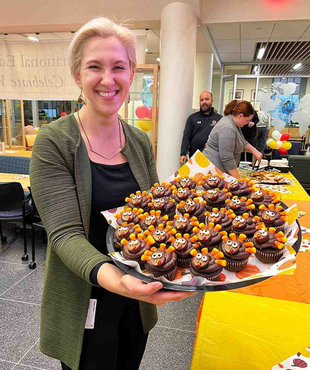 woman holds platter of cupcakes decorated like turkeys