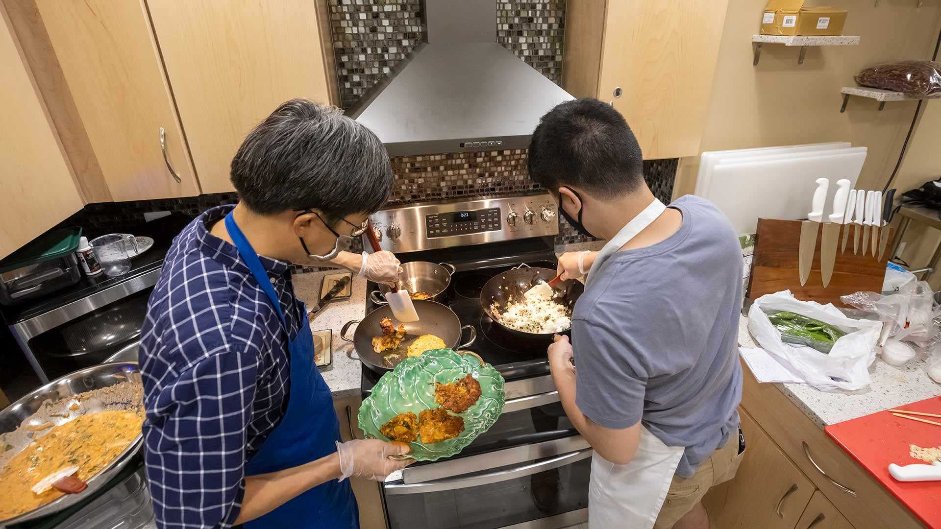 Two men cook kimchi pancakes and kimchi fried rice on a stove