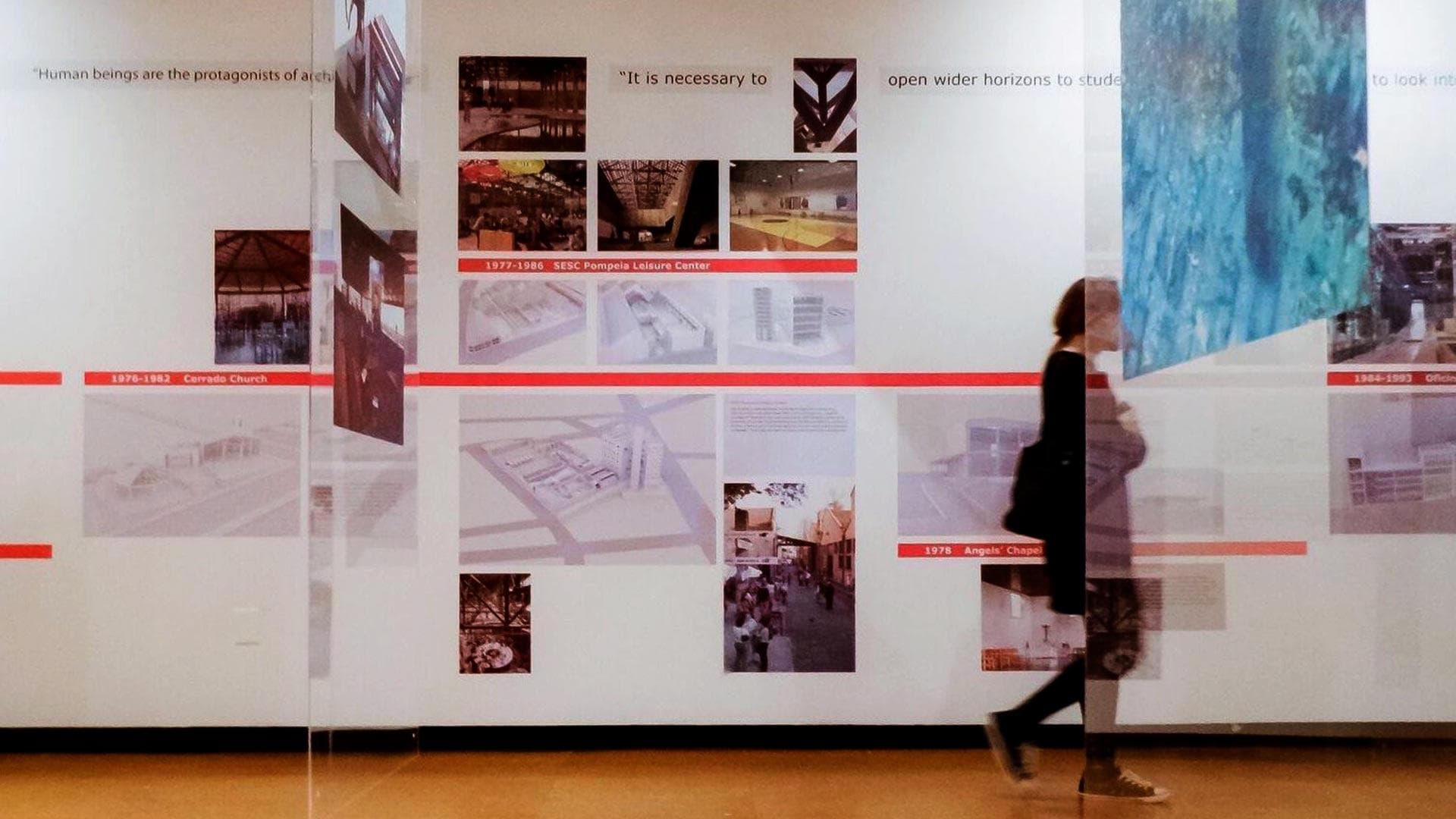 visitor walks past photos on wall as part of “Lina Bo Bardi: To Teach Is to Construct” exhibition