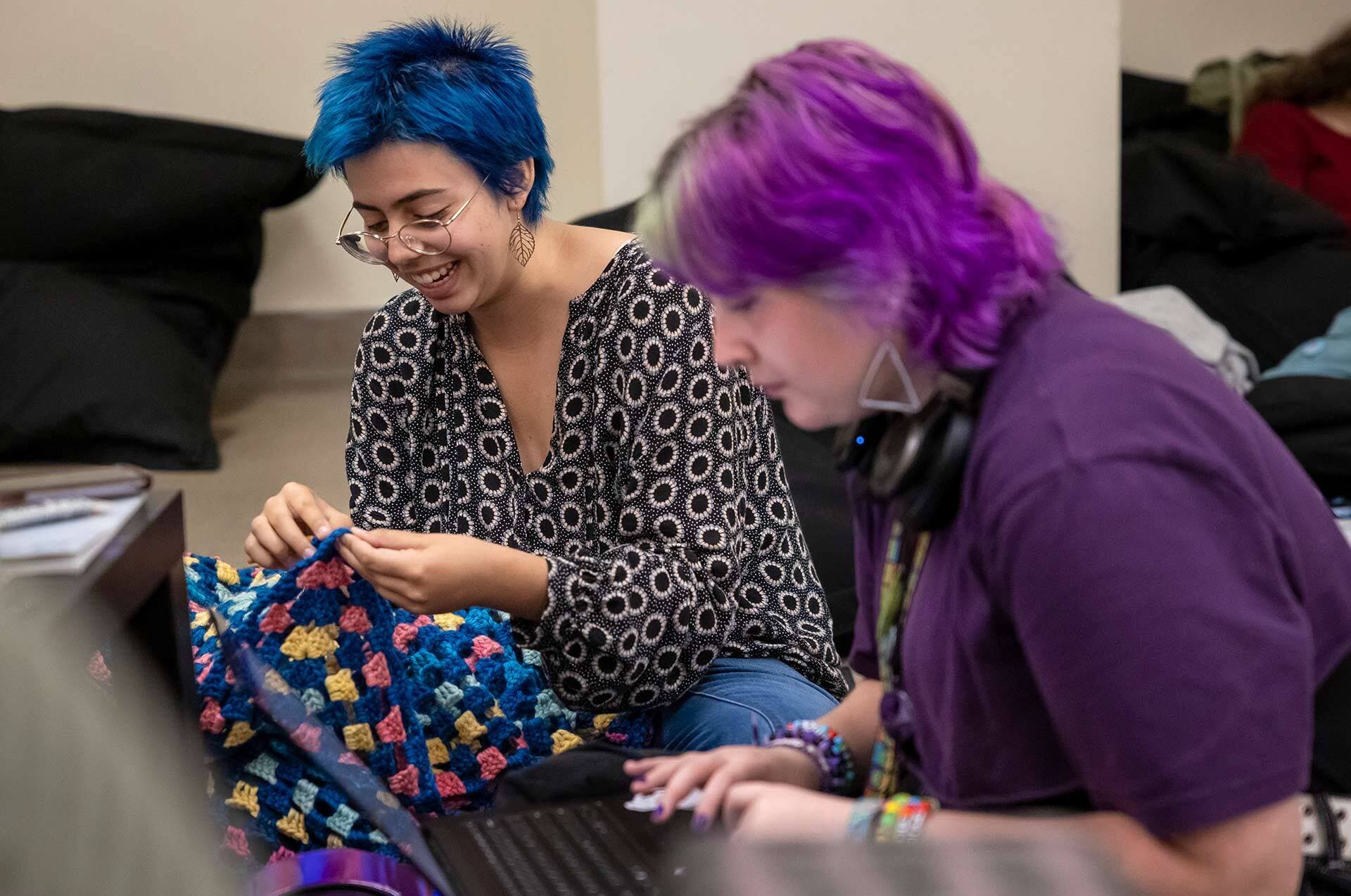 students with blue and purple hair smile over a colorful cloth and laptop