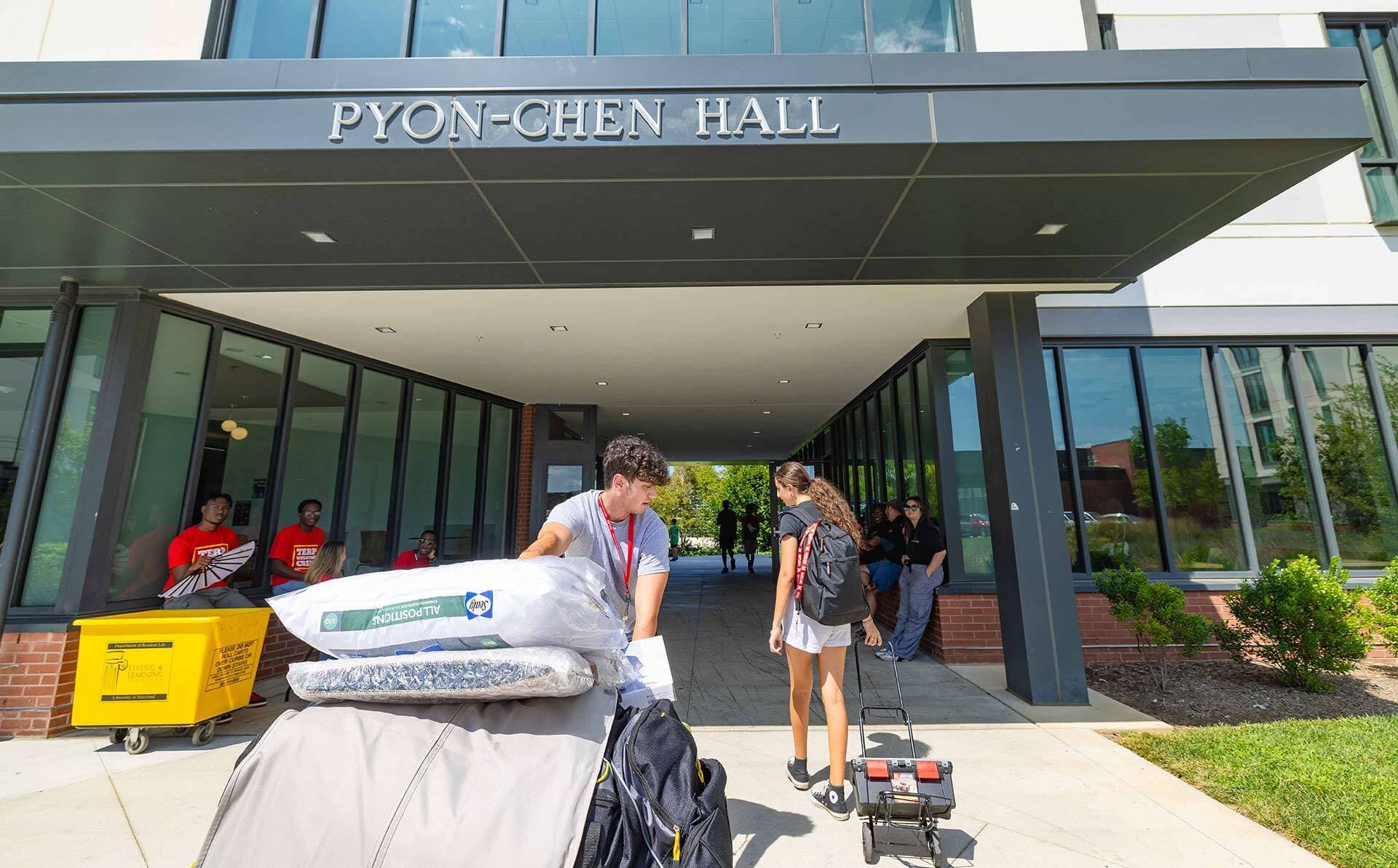student pulls a giant pile of belongings under the sign above the door of pyon-chen hall
