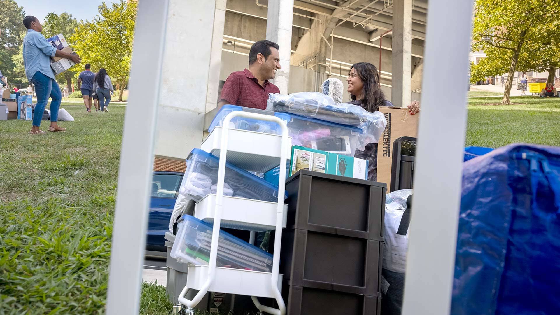 father and daughter stand near giant pile of possessions, preparing to move into a dorm