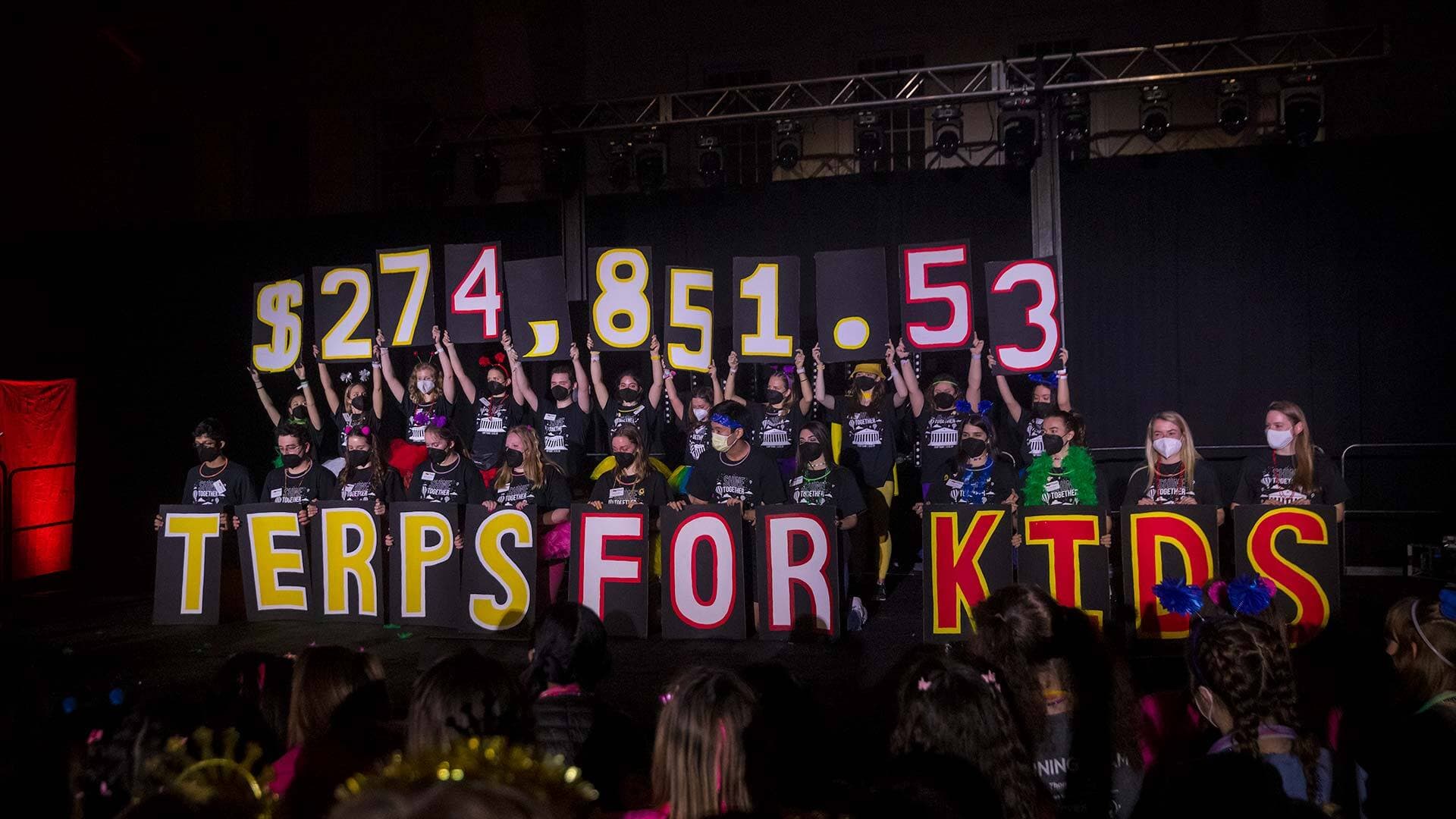 Terp Thon participants onstage hold aloft signs showing total money raised
