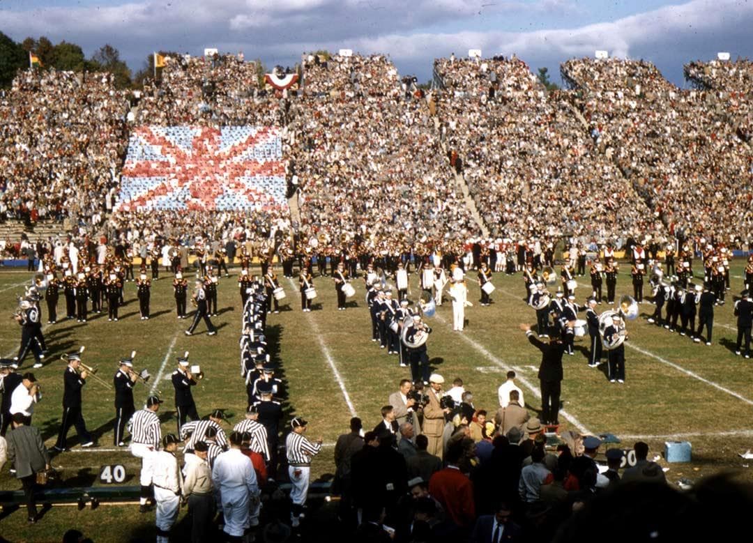 band marches on the field while fans hold up cards to form Union Jack in the stands