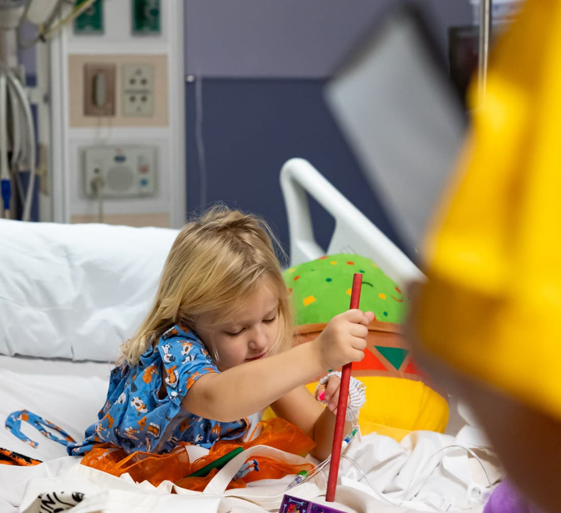 Pediatric hospital patient plays musical instrument on hospital bed