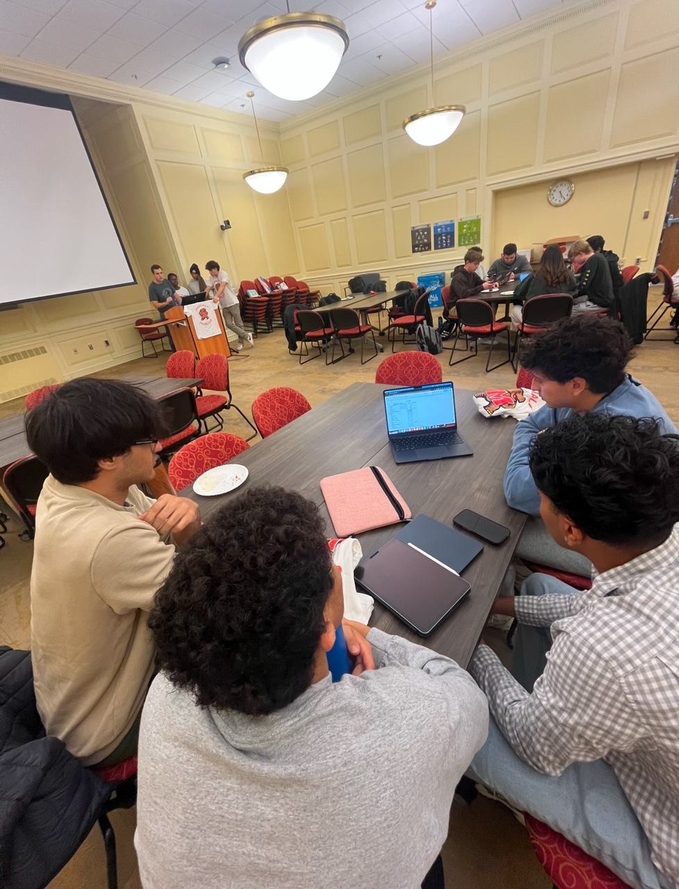 Students look at a spreadsheet on a laptop as they sit around a round table