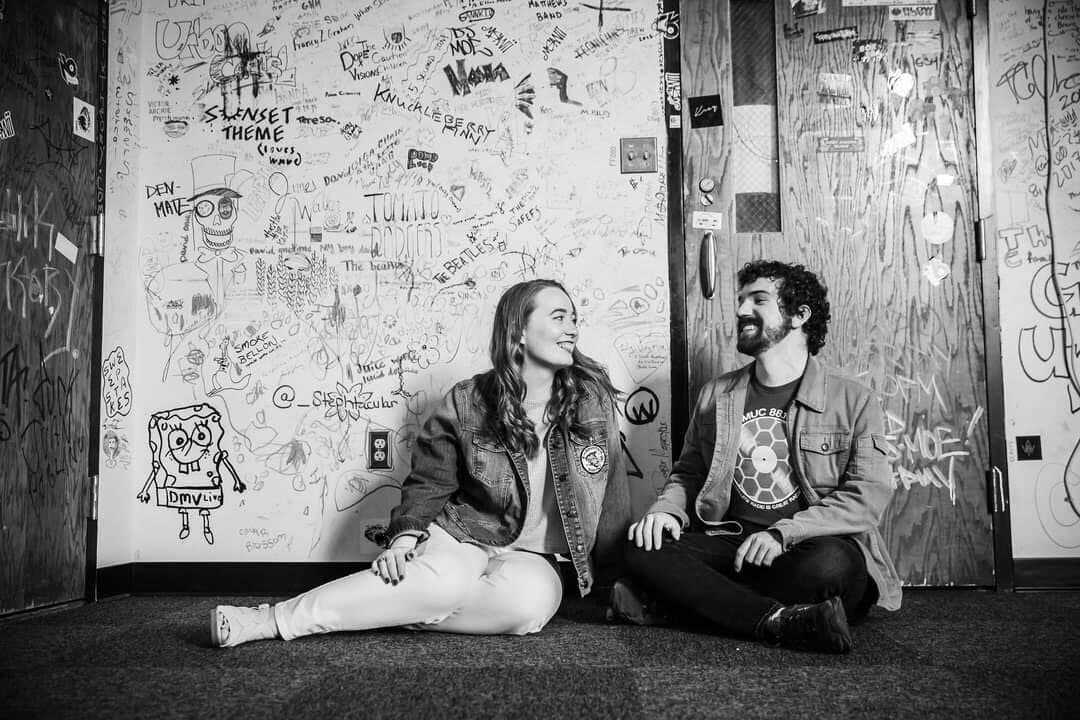 couple sits at radio station in front of graffitied walls